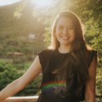 A young woman smiling in a natural outdoor setting during the golden hour.