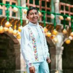 Man in traditional embroidered shirt poses outdoors with festive decor. Bright, cultural atmosphere captured.